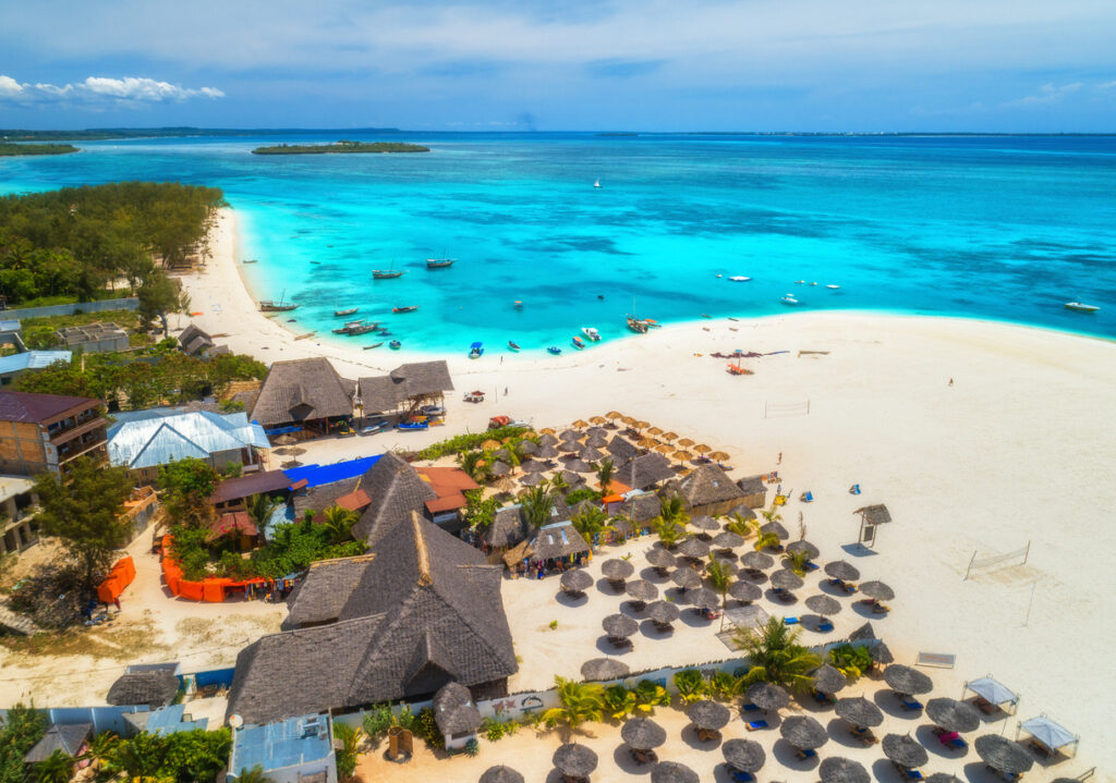aerial view of tropical sandy beach with palms and umbrellas at sunny day. summer holiday. landscape with palm trees, hotels, buildings, white sand, boats and yachts in azure sea. view from above